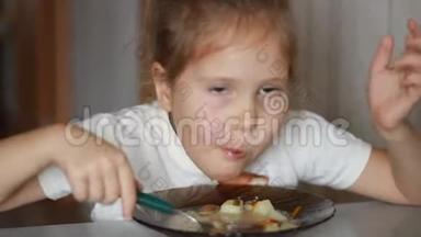 孩子用<strong>勺子</strong>汤吃饭。 午餐结束了<strong>一个</strong>小女孩坐在家里做饭和吃食物的桌子上的肖像。